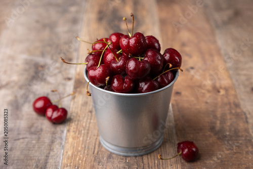 Juicy ripe fresh cherries with water drops in a miniature bucket on a wooden background. Seasonal fruits, harvest, in rustic style. Selective focus, close-up.
