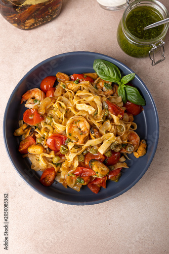 Noodles with shrimps, mussels, tomatoes, onions and capers. Pasta is served with olive oil and pesto sauce. Homemade traditional Mediterranean cuisine. Selective focus, close-up.