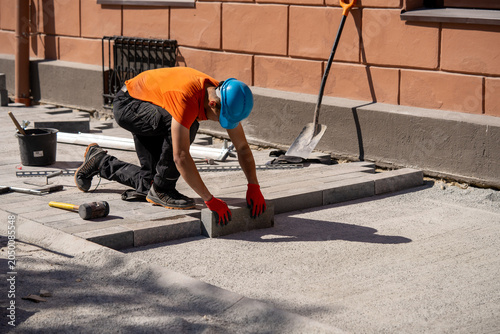 Construction worker laying paving stones on outdoor pathway near building with tools and materials