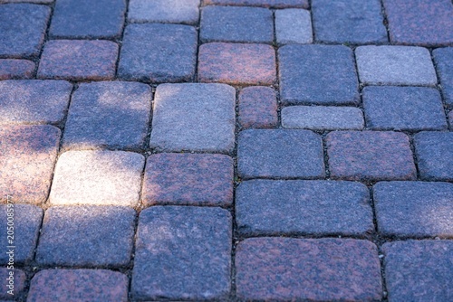 Textured cobblestone pavement with varying shades of gray and pink stones in sunlight