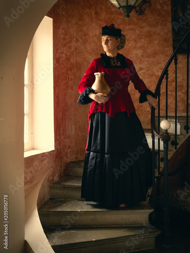 Victorian lady in red bustle dress on stairs
