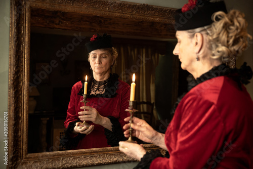 Victorian lady in red bustle dress holding candle