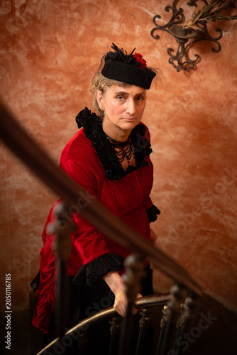 Victorian lady in red bustle dress coming up stairs