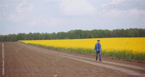 Farmer standing beside blooming crop fields on a rural dirt road