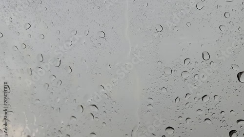 Close-up of water droplets and rain streaks on a clear glass window surface against a gray, overcast background.