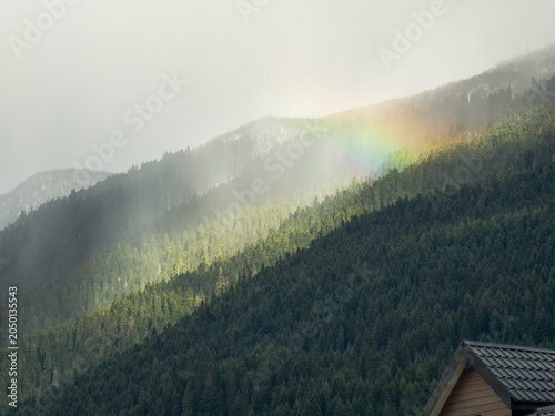 Misty mountains rise beneath a soft, glowing sky, rainbow.