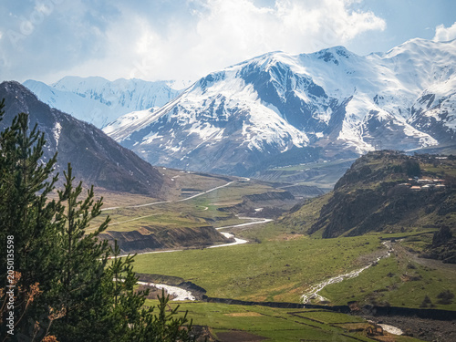 Snow-capped peaks rise above lush green valleys, Kazbegi region.