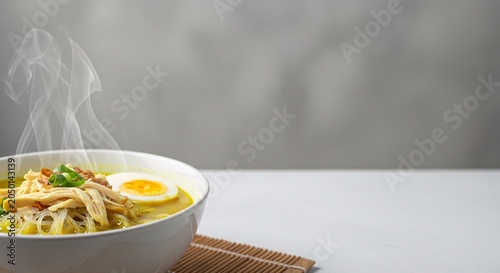 Steaming bowl of noodles with coriander seeds and egg on a table indoors
