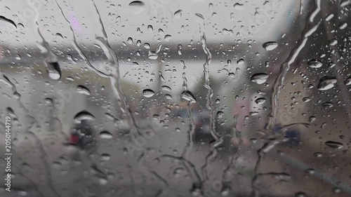 Heavy rain droplets and streaming water on a glass window with a blurred city street background on an overcast day.