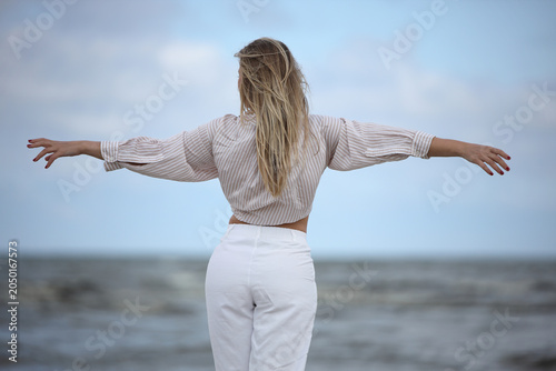 Woman standing on beach with arms outstretched facing sea
