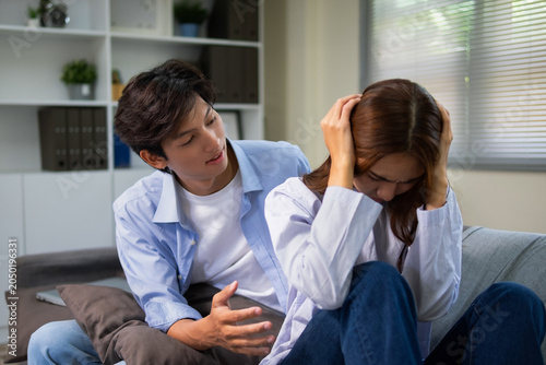 The young couple are at home during a tense time. The woman sits with her arms crossed and a sullen expression while her partner tries to explain the conflict.