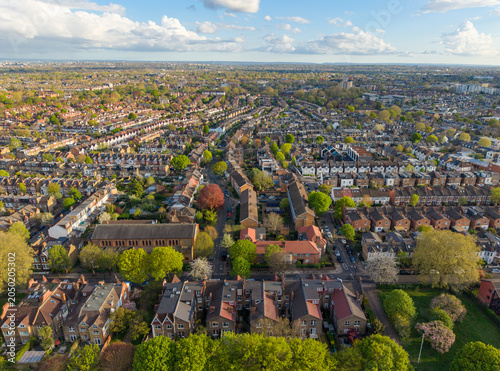 LONDON, UK - JUNE 9, 2026: High-angle panoramic drone view of a vast suburban neighborhood with terraced houses, lush green trees, and the horizon under summer clouds