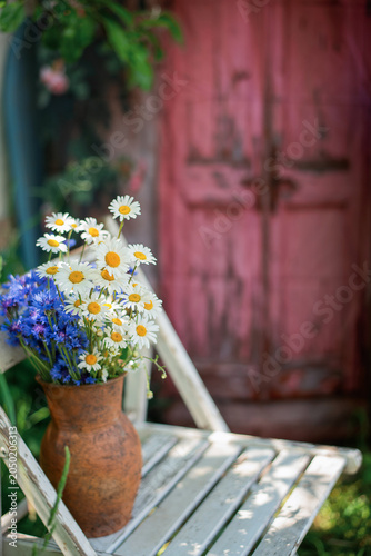 Summer bouquet of daisies and cornflowers in a rustic clay vase on a chair