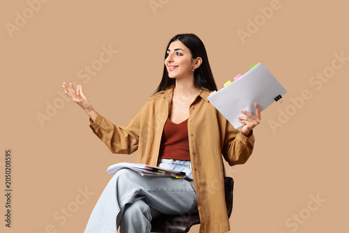 Young actress with film script sitting on beige background