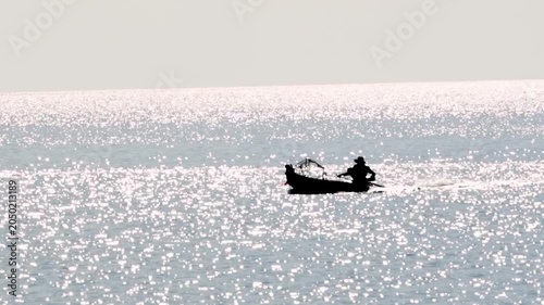 Silhouetted fisherman glides across shimmering water. Sunlight dances off the waves, creating a dazzling surface. The lone boat drifts peacefully, untouched by wind or current. Stillness suggests calm