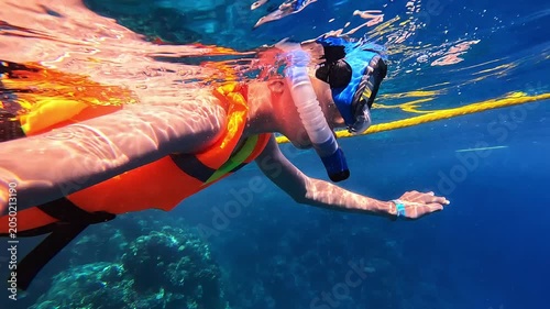 Person snorkels under water, wearing life jacket. Blue water ripples around them. Dive mask and fins complete their gear. Sunlight filters through the surface