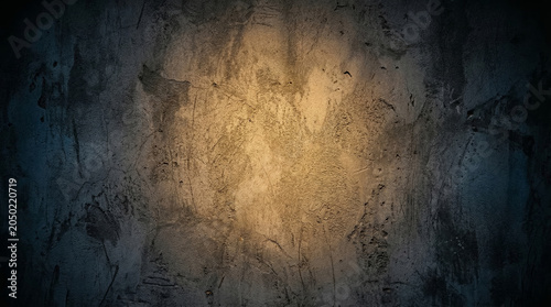 Dark grunge concrete wall texture with warm golden brown spotlight center and dark blue vignette background