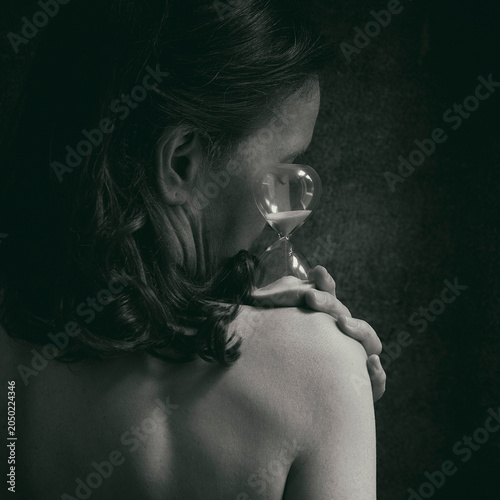 Woman with her back to the camera holding an hourglass in her hands, symbolizing the passage of time