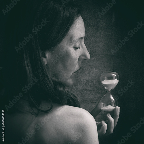 Woman with her back to the camera holding an hourglass in her hands, symbolizing the passage of time II