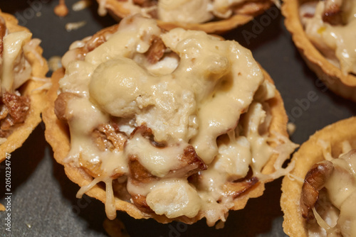 Homemade tartlets filled with chanterelle mushrooms and chicken pieces stewed in cream, topped with grated cheese after baking in oven. Close-up of a festive appetizer cooking process.