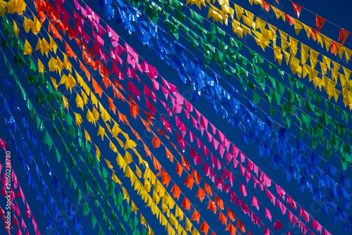 Fileiras cheias de bandeirolas coloridas de Festa Junina cruzando o céu azul.