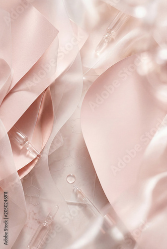 A collection of soft pink fabric pieces and clear glass droppers is arranged on a light surface. The scene captures a creative workspace filled with gentle tones and textures