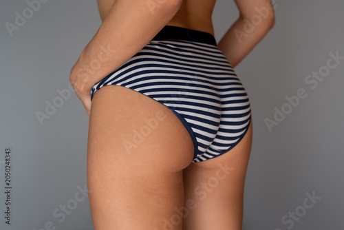 Foto Back view of a young woman wearing striped cotton panties, showing shapely buttocks, smooth skin and firm body on a grey background