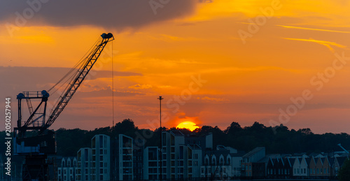 Bilde på lerret Orange sunset with the sun halfway below the horizon behind houses, creating a warm evening sky and dramatic silhouette