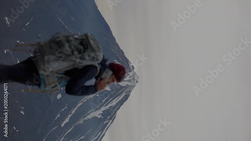 Man with large backpack stands against backdrop of majestic volcano with an icy peak and slopes of solidified lava. Back view. vertical video
