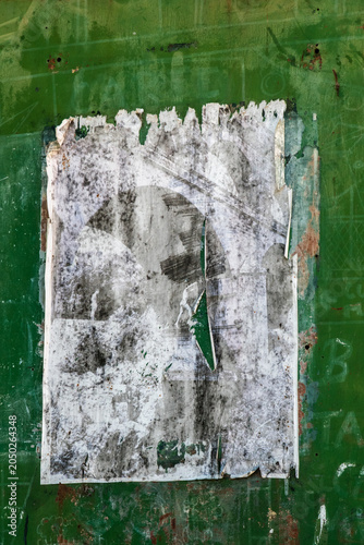 A torn and weathered peeling poster remnant on a vivid green painted wall, creating an abstract textured urban art composition, France