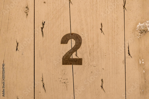Photos A rustic metal number 2 affixed directly onto a weathered, natural wood plank do
