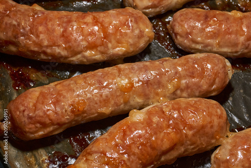 Hot homemade sausages with a juicy texture and golden surface on a parchment-lined baking tray. Golden Brown Pork Sausages Fresh from the Oven. Baked Homemade Sausages Close Up.