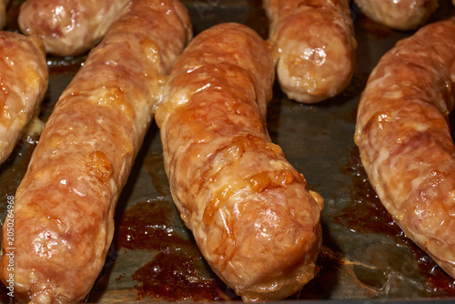 Hot homemade sausages with a juicy texture and golden surface on a parchment-lined baking tray. Golden Brown Pork Sausages Fresh from the Oven. Baked Homemade Sausages Close Up.