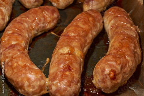 Hot homemade sausages with a juicy texture and golden surface on a parchment-lined baking tray. Golden Brown Pork Sausages Fresh from the Oven. Baked Homemade Sausages Close Up.