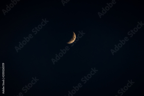 A glowing golden crescent moon hangs against a deep, dark blue-black night sky, creating a minimal and serene celestial scene