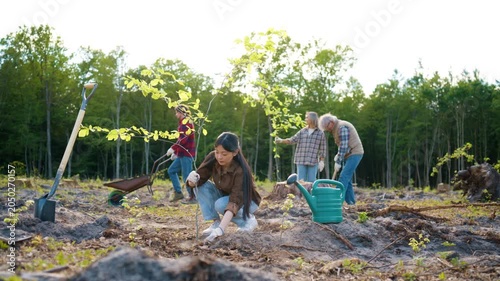 Asian woman planting tree sapling during environmental restoration project. Female volunteer kneeling and covering roots with soil on cleared woodland area. Eco conservation work. Forest regeneration.
