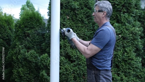A construction worker uses a power tool to strip paint from a pole.