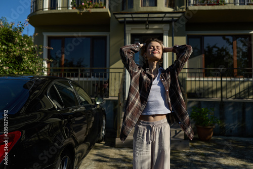 Fotografi Young woman outdoors, arms raised in a sunlit moment, wearing a plaid shirt and