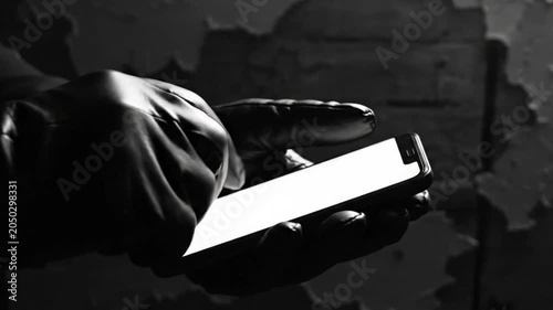 Black and white shot of gloved hands using a smartphone in a dimly lit setting