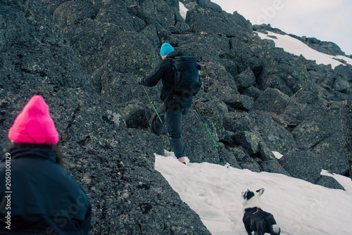 Hikers with backpack and dog climbing rocky snow slope