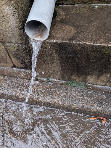 Rainwater Flowing from Urban Drainpipe onto Wet Pavement During Heavy Rainfall Weather Conditions