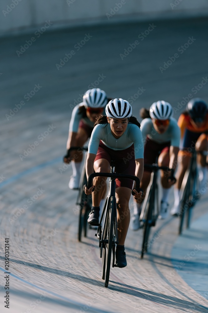 Fototapeta premium Competitive track cycling team racing on a banked velodrome curve for sports banner background and athletic training design