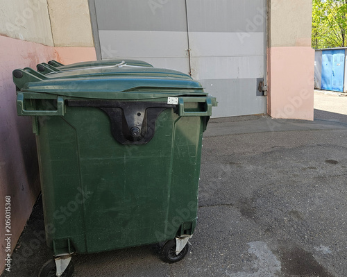 Green waste dumpster behind office building on city street, commercial garbage disposal, urban sanitation service