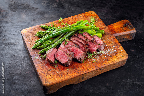 English medium broiled tagliata di manzo beef steak meat with grilled green asparagus served as close-up on rustic wooden board