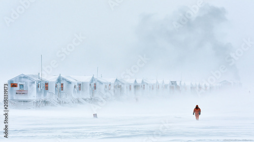 Extreme Weather Adventure: Solitude in a Snowy Arctic Landscape with Fishing Huts and Storm Clouds