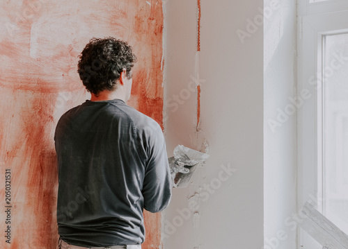 Bild auf Leinwand A Caucasian young man is putting putty on the wall.
