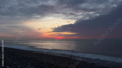 Sunset casts vibrant colors across the ocean waves, creating a serene atmosphere at the beach with pebbles along the shoreline