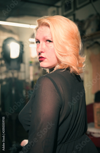 This captivating portrait features a woman with striking makeup and flowing blonde hair, exuding elegance and intrigue in an artistic studio environment with soft lighting.