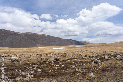 Vast Rocky Alpine Tundra Valley with Golden Steppe and Dark Mountain Ridge Under Dramatic Clouds, Mongolian Altai