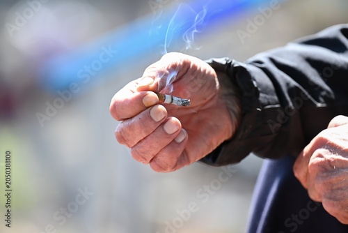Photos Close up of wrinkled hand holding burning cigarette with smoke showing bad tobac